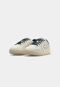 Hvite mokkasinsneakers med marineblå snørebånd, rund tå og beige gummisåle. Har en logodetalj på siden.