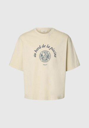 Krém színű rövid ujjú póló kerek nyakkivágással, tengerészkék francia szöveggel és egy kör alakú hal grafikával egy medencében.