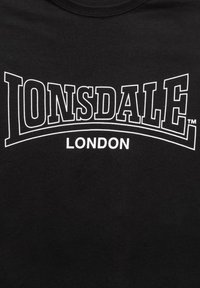 Melnas kokvilnas T-krekls ar kontrastējošu balto tekstu "LONSDALE" izliekti virs "LONDON", ar preču zīmes simbolu labajā pusē.