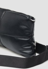 Schwarze Lederhandtasche mit texturiertem Oberfläche, Reißverschluss und verstellbarem schwarzen Gurt für den Crossbody-Tragekomfort. Abgerundete Form mit sanften Kanten.