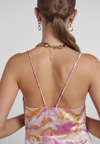 Robe en satin avec un motif abstrait rose, jaune et blanc. Elle présente des bretelles fines et un dos en V, agrémentés d'un collier en chaîne dorée.