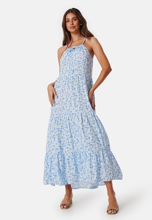 Robe maxi en tissu bleu clair avec un petit motif floral, présentant un design à volants, des bretelles fines et un détail en nœud au niveau du décolleté.