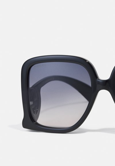 Gafas de sol negras de gran tamaño con lentes degradados. Acabado mate, diseño de montura cuadrada y un sutil logo en la parte superior izquierda de la lente.
