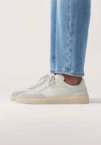 Weiße Ledersneaker mit grauen Wildlederakzenten, flacher cremefarbener Gummisohle und runden Schnürsenkeln. Lässiges Design, sichtbare Nähte und durchbrochene Details.