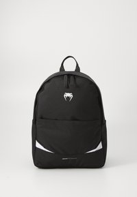 Mochila negra hecha de un tejido duradero, con un bolsillo frontal, acentos blancos y un asa superior. Logo visible en la parte frontal.