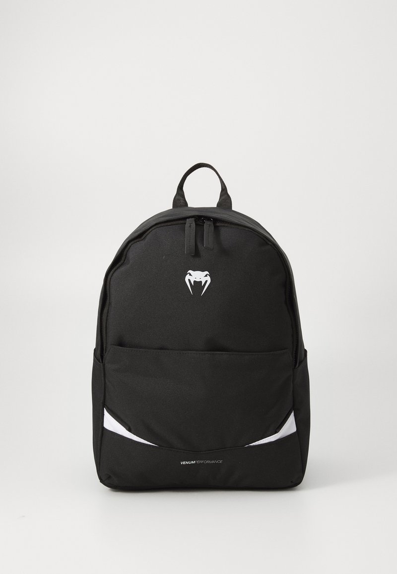 Mochila negra hecha de un tejido duradero, con un bolsillo frontal, acentos blancos y un asa superior. Logo visible en la parte frontal.