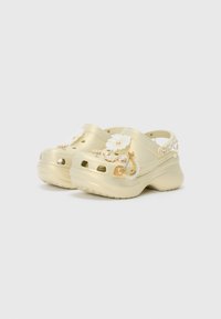 Gold-colored clogs with floral and decorative embellishments. Features ventilation holes, textured surface, and a chunky outsole.