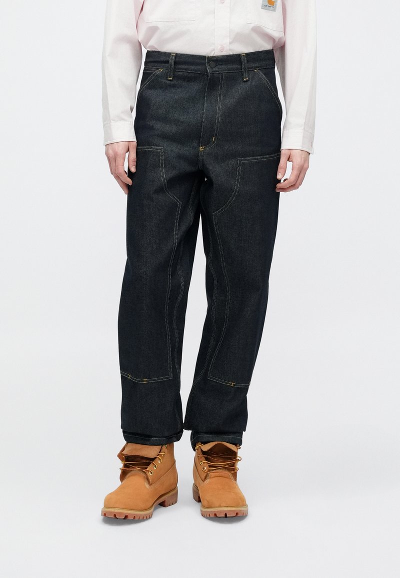 Mörkblå jeans med gul söm, rak skärning och femficksdesign, kombinerade med beige snörstövlar för arbete.