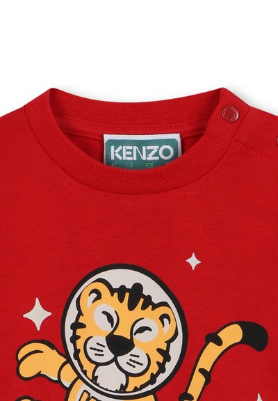 Czerwona bawełniana koszulka z grafiką tygrysa w hełmie kosmicznym i wesołymi gwiazdami. Okrągły dekolt z guzikami.