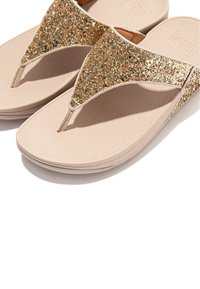 Tongs beiges avec une semelle texturée et une lanière dorée scintillante, présentant un design à brides entre les orteils et un coussin de pied doux pour plus de confort.