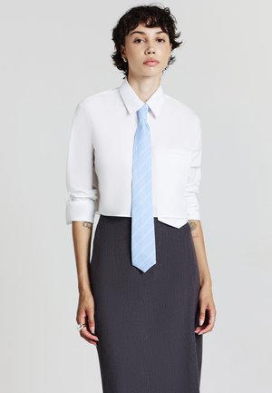 Camicia bianca tagliata con colletto, abbinata a una gonna a matita grigio scuro strutturata. Accessoriata con una cravatta a righe blu chiaro.