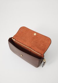 Braune Leder-Clutch mit offenem oberen Klappen, die ein weiches Wildleder-Innenfutter und ein goldenes Reißverschlussfach im Inneren zeigt.