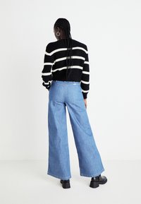 Zwart-wit gestreepte gebreide trui gecombineerd met lichtblauwe wijde jeans. Opvallende details zijn de geribbelde textuur en de cropped snit.