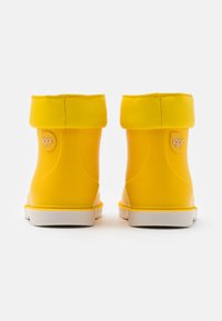 Bottes en caoutchouc jaunes avec un bout arrondi, une semelle blanche et un revers roulé. Présente un petit logo 'igor' sur le côté. Texture lisse.