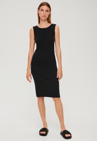 Robe noire sans manches en matière bodycon avec une texture côtelée et un col rond, portée avec des sandales noires à enfiler avec des détails tissés.