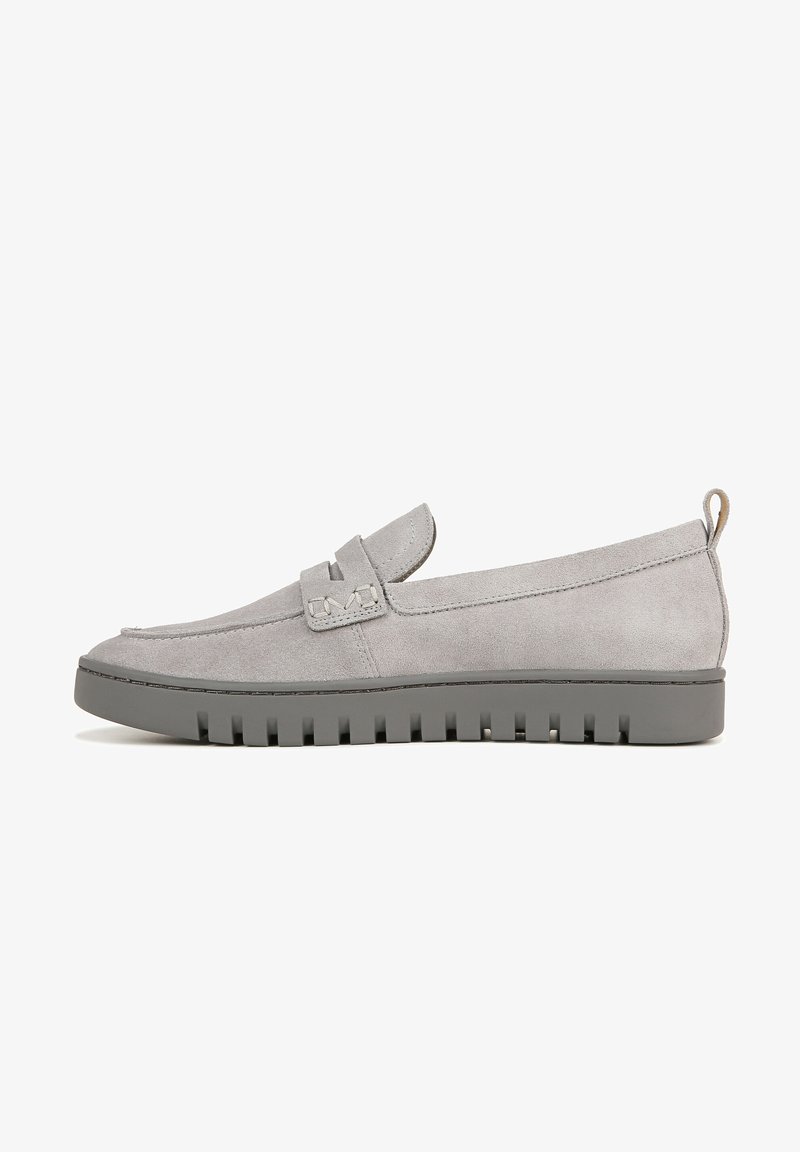 Mocassins en daim gris avec une semelle en caoutchouc plate, ornés d'une bride décorative et de détails de couture. Le design est élégant et minimaliste.