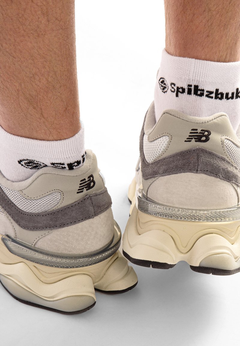 Klobige graue und cremefarbene New Balance Sneaker mit Mesh- und Wildlederdetails, transparenten Akzenten und einer markanten gebogenen Sohle.
