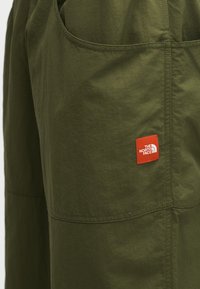 Κοντινό πλάνο σε ύφασμα ελιάς με ορατές ραφές και ένα μικρό κόκκινο ορθογώνιο ταμπελάκι με το λογότυπο The North Face.