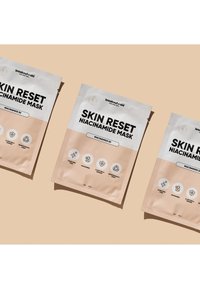 Verpackung der Skin Reset Niacinamide Maske mit hellrosa Hintergrund, schwarzem fettem Text, Symbolen und einem Label für biologisch abbaubare Materialien.