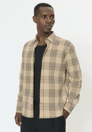 Chemise à carreaux beige avec lignes noires, style boutonné, une poche poitrine, manches longues et tissu léger texturé.