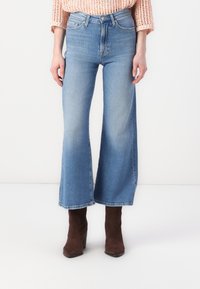 Széles szárú kék farmernadrág magas derekával, világos mosással, finom kopással és középhosszan vágott szegéllyel.