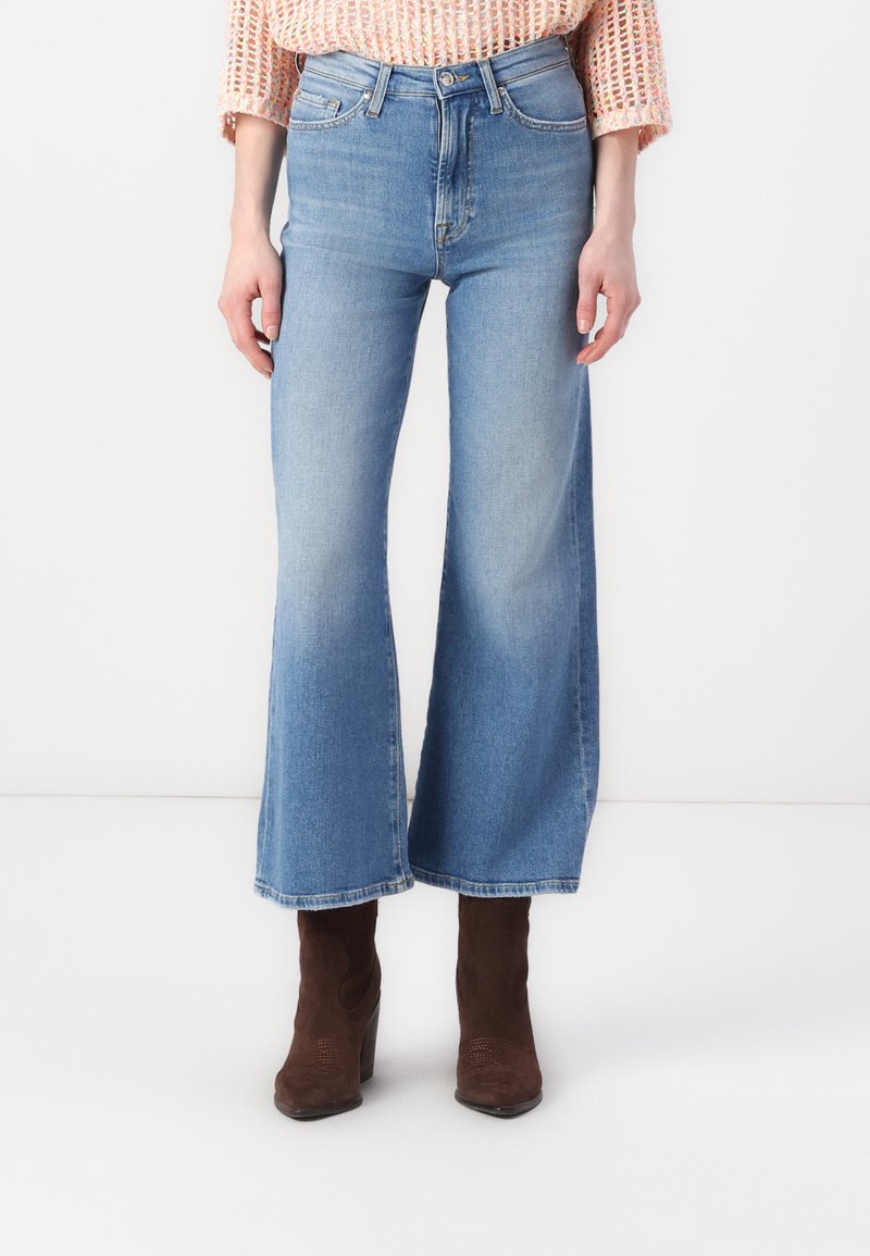 Széles szárú kék farmernadrág magas derekával, világos mosással, finom kopással és középhosszan vágott szegéllyel.