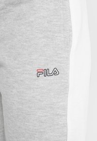 Grauer Sweatshirtstoff mit einem weißen Seitenpaneel; präsentiert ein FILA-Logo in Schwarz und Rot in der unteren rechten Ecke. Glatte Textur, lässiges Design.