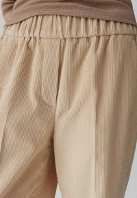 Pantaloni in tessuto a coste beige con cintura elastica e tasche laterali, che mostrano una texture morbida e righe verticali.
