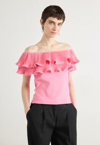 Top ajustado rosa con escote off-the-shoulder y volantes plisados en el cuello. Tela suave, diseño sencillo, combinado con pantalones negros.