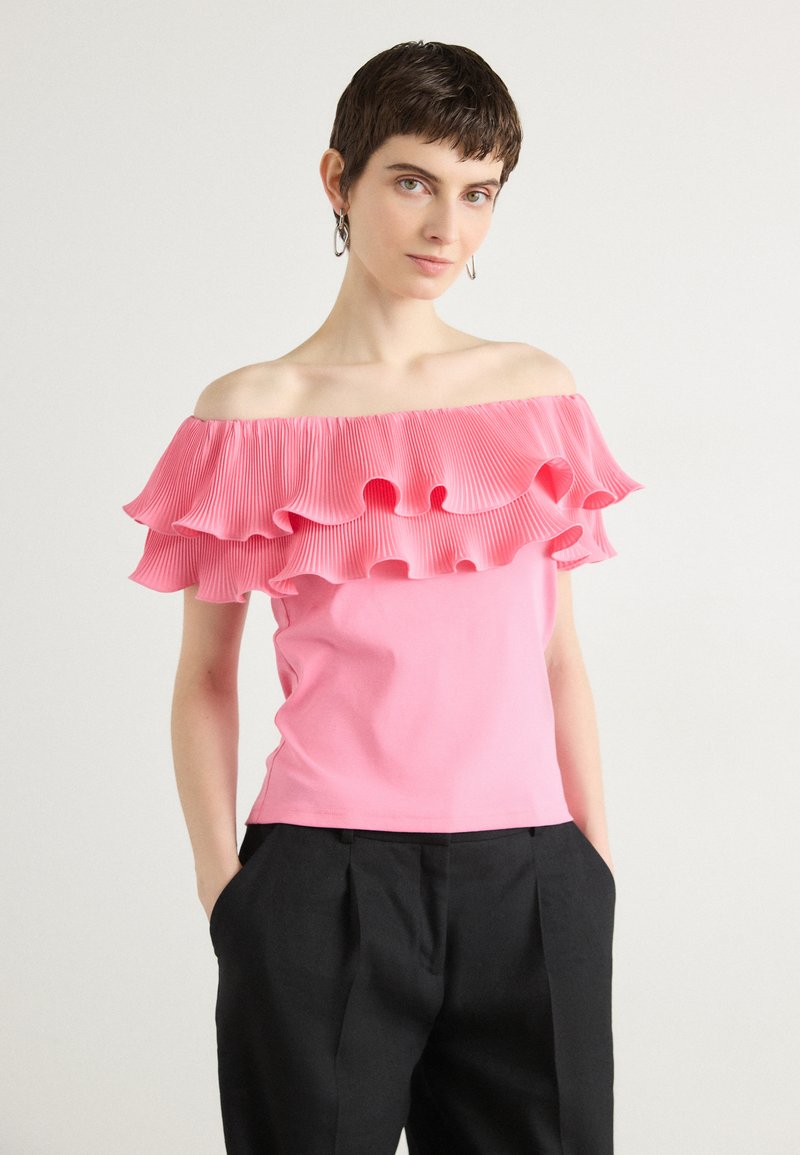 Top ajustado rosa con escote off-the-shoulder y volantes plisados en el cuello. Tela suave, diseño sencillo, combinado con pantalones negros.