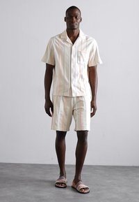 Leichtes, gestreiftes Kurzarmhemd und passende Shorts in Creme mit orangefarbenen Linien. Verfügt über eine Brusttasche und einen lockeren Schnitt.