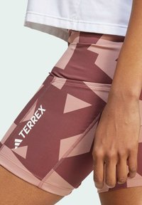 Terrex patterned shorts in shades of brown and pink feature geometric designs, sleek fabric, and an athletic fit with prominent branding.