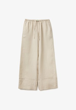 Beżowe spodnie o szerokich nogawkach z elastycznym paskiem i sznurkiem, wyposażone w boczne kieszenie oraz przeszycia na dole.