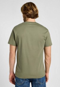 Oliwkowa koszulka z krótkim rękawem i okrągłym dekoltem, o gładkiej fakturze, w połączeniu z niebieskimi dżinsami, wyświetlona z tyłu.