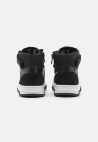 Bottes noires à la cheville en suède et matériau synthétique, avec une fermeture éclair, une semelle intermédiaire blanche et des accents texturés au niveau du talon.