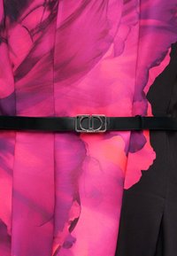 Robe rose et noire à imprimé floral. Elle possède une ceinture en cuir noir avec une boucle argentée. Texture lisse, tissu fluide.