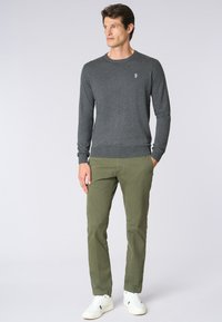 Maglione grigio a maglia con scollatura rotonda, polsini e orlo a costine, abbinato a pantaloni chino verde oliva e sneakers bianche. L'articolo ha un tessuto texturizzato.