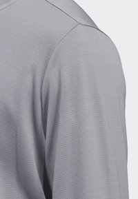 T-shirt de sport gris avec un tissu texturé et respirant doté d'un motif subtil. Le design comprend un col lisse et des coutures d'épaule.