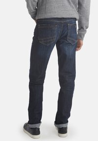 Mørkeblå denimjeans med slim fit, med lett teksturert stoff, kontrastsømmer og fem-lommers design. Rullet opp i anklene.