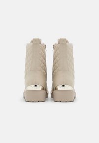 Bottines beiges matelassées avec des accents de talons en métal doré, présentant une finition texturée et des fermetures à glissière latérales doubles pour un enfilage facile.