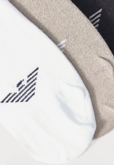 Τρία διπλωμένα ζευγάρια κάλτσες σε λευκό, μπεζ και μαύρο, κάθε ένα με ένα στυλιζαρισμένο λογότυπο πουλιού κοντά στη μανσέτα.