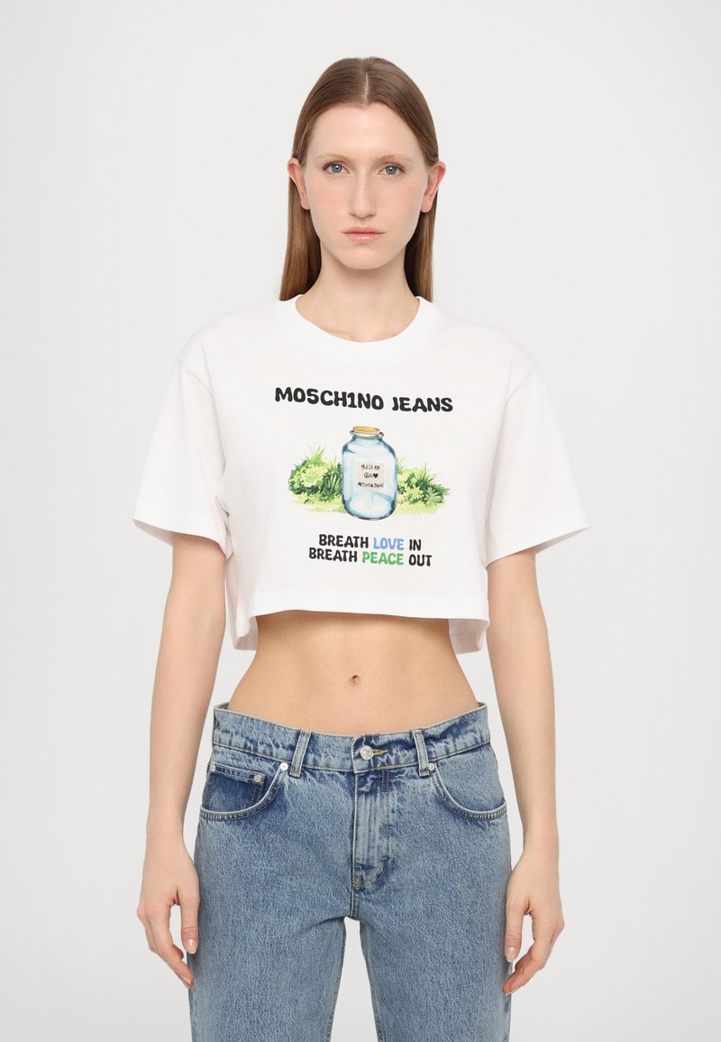 Hvit kort t-skjorte med "MOSCHINO JEANS" tekst og grafikk av et glass; kombinert med lyseblå, høyt midje denimjeans.