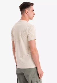 Beige T-shirt med et diskret prikmønster, korte ærmer og rund hals; lavet af blød, åndbar stof.