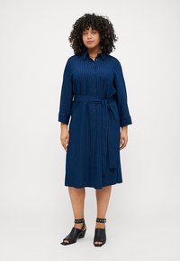Abito camicia blu navy con bottoni, a righe orizzontali, cintura in vita e maniche a tre quarti. Tessuto morbido e lunghezza fino al ginocchio.