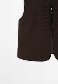 Donkerbruin vest met een gladde textuur, voorzien van verticale stiksels en een rij decoratieve zilverkleurige knopen aan de voorkant.