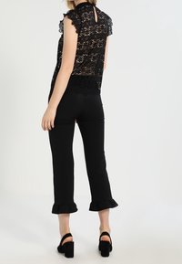 Musta pitsitoppi, jossa on kukkakuosi ja hihattomat hihat, yhdistettynä mustiin istuviin housuihin, joissa on röyhelöhuput. Malli näkyy takaa.