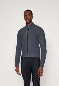 Chaqueta de ciclismo gris con un cuello alto, cremallera frontal completa y acentos en color teal contrastante. Textura suave y diseño ajustado.