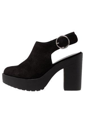 Czarne zamszowe sandały na platformie z zaokrąglonym noskiem, piętą z paskiem w stylu slingback oraz okrągłym srebrnym akcentem w postaci pierścienia. Gruba, kwadratowa obcas.