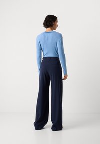 Helles blaues geripptes Sweatshirt mit langen Ärmeln, kombiniert mit navy-blauen weiten Hosen mit Gesäßtaschen. Minimalistisches Design, glatte Textur.