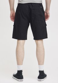 Zwarte cargoshorts van katoen, met zijzakken en een achterzak, met een ontspannen pasvorm en een lengte tot de knie. Gemaakt met zwarte sneakers.